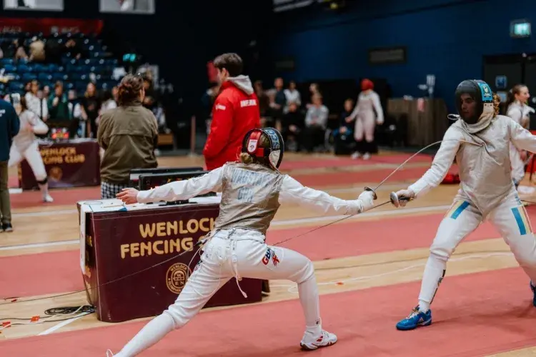 girl fencing, with sword touching chest of competitor